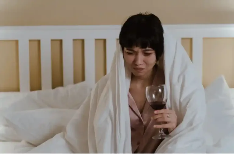Žena s kocovinou držící sklenku vína v posteli