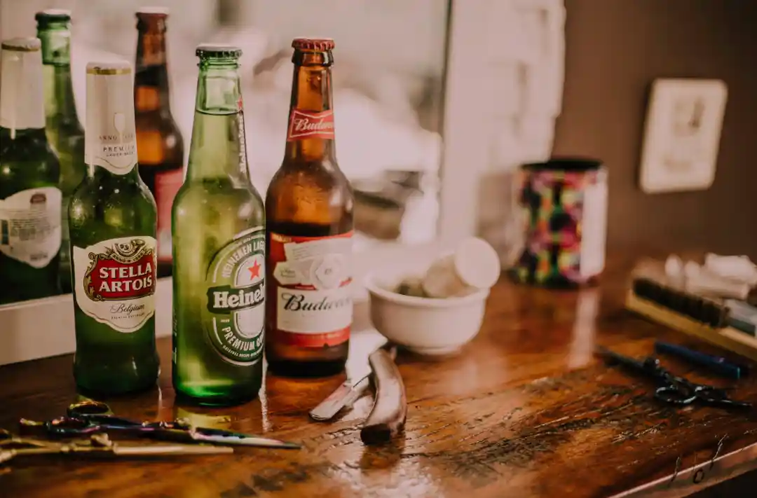 Skleněné lahve piva Stella Artois, Heineken a Budweiser na stole vedle nástrojů